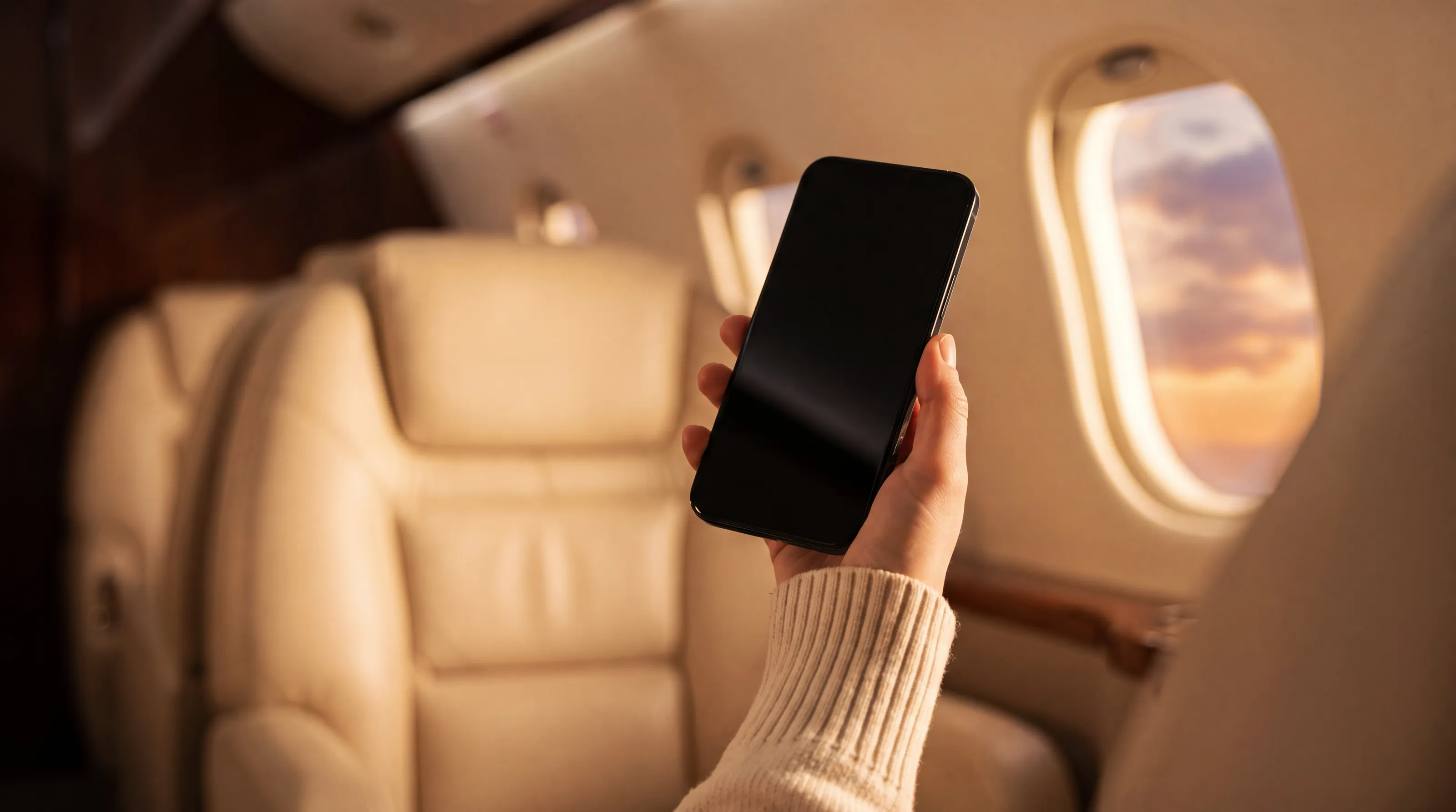 A hand holds a phone with the Veltracon member app in a private jet cabin at golden hour