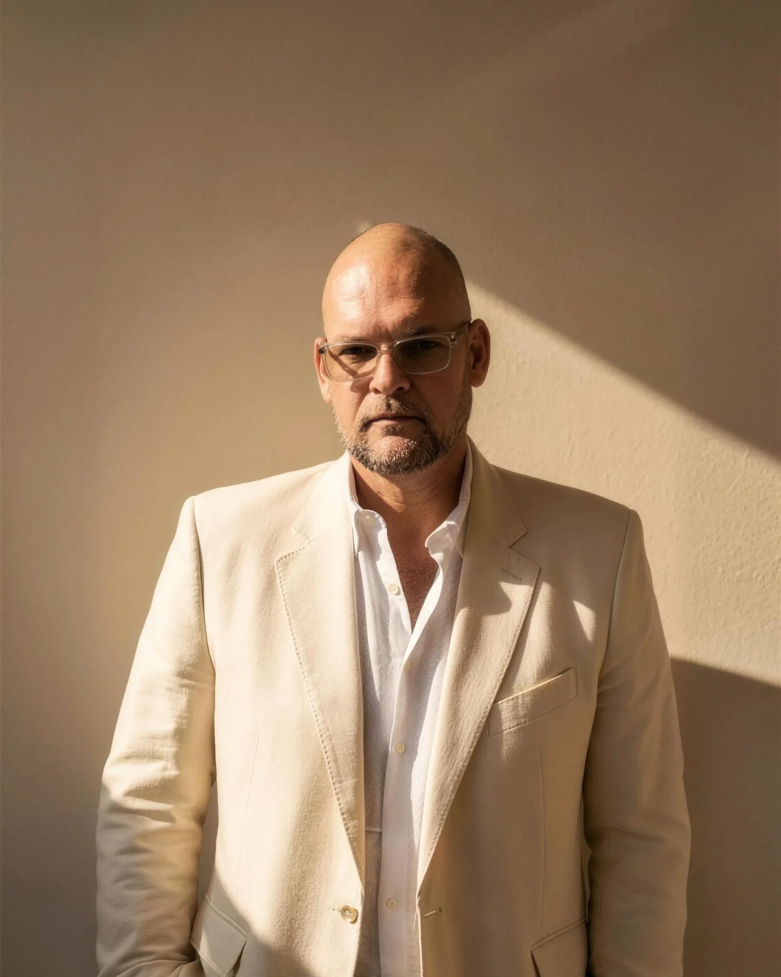 Patrick Gruhn in a light suit against a sunlit wall